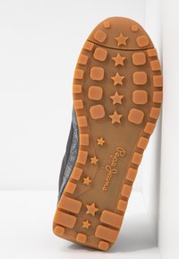 Semelle de basket noire avec bande de roulement en caoutchouc orange présentant des formes d'étoiles et de carrés, et logo "Pepe Jeans London" embossé au centre.