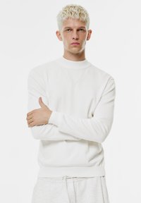 Weißer Pullover mit Rundhalsausschnitt und langen Ärmeln, gefertigt aus einem weichen, strukturierten Stoff. Gerippte Bündchen an Ärmeln und Saum sorgen für einen figurbetonten Sitz. Dezente Designdetails.