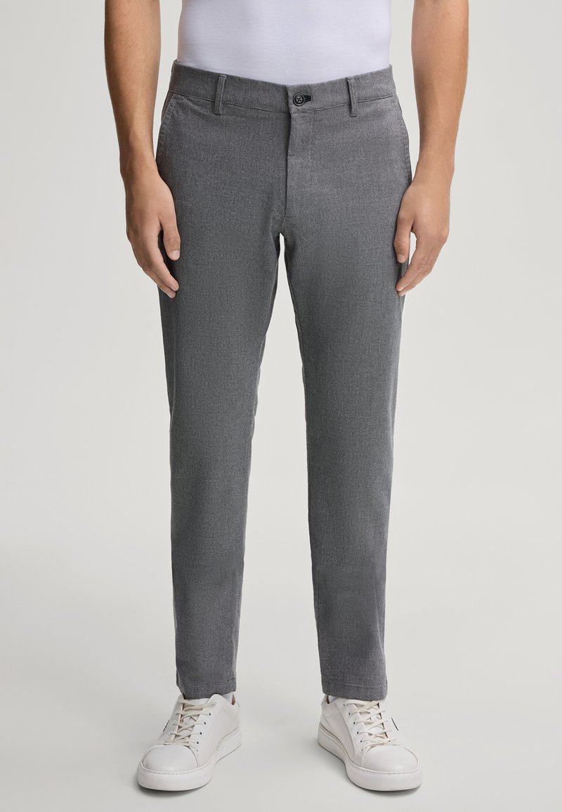 Pantaloni grigi, con una texture e una vestibilità slim, dotati di tasche laterali, chiusura a bottone e una cintura pulita, abbinati a sneakers bianche.