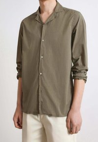 Olive green button-up shirt with a checkered pattern, featuring a collar, long sleeves, and rolled cuffs, made of a lightweight fabric.
