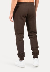 Brązowe spodnie dresowe o luźnym kroju, z elastycznym pasem i ściągaczami na nogawkach. Wykonane z miękkiej tkaniny, zestawione z białymi sneakersami.
