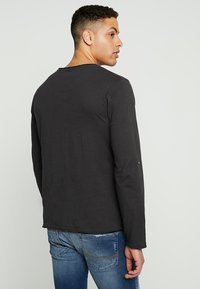 Zwarte longsleeve gemaakt van zachte stof, met een ronde hals, minimale stikdetails en een relaxed fit.