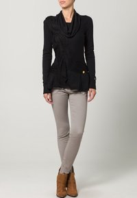 Schwarzer Strickpullover mit drapekragen und strukturiertem Muster. Kombiniert mit hellgrauen, enganliegenden Hosen und braunen Stiefeletten.