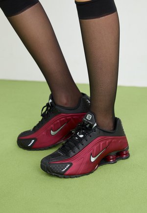 Zwarte en bordeauxrode sportschoenen met een gestructureerde bovenkant, met veters en een hiel met zichtbare luchtkussens. Voorzien van een zilveren Nike swoosh-logo.