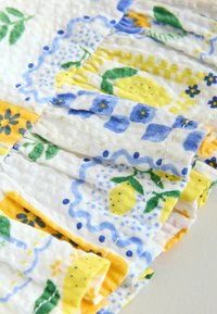 Gros plan d’un tissu blanc avec des citrons jaunes, des feuilles vertes et des motifs floraux bleus dans un design matelassé texturé.