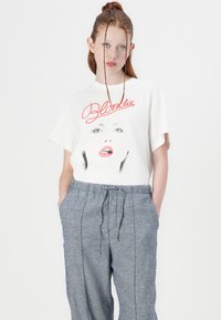 Hvid t-shirt med et grafisk motiv af et ansigt med røde læber og teksten "Blondie". Matchet med grå, løstsiddende bukser med snøre.