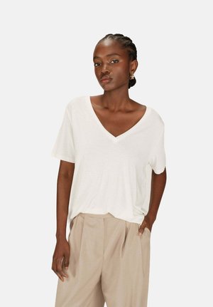 T-shirt blanc à col en V, fabriqué en tissu doux, avec des manches courtes et une coupe décontractée, associé à un pantalon beiges taille haute.