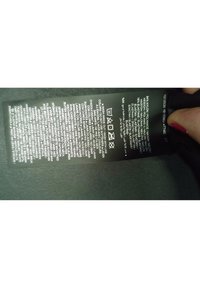 Étiquette d'entretien des vêtements avec symboles de lavage et composition du tissu comprenant du nylon, polyamide et élasthanne en plusieurs langues, tenue par une main.