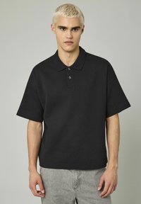 Polo shirt noir à manches courtes avec une coupe décontractée, un col classique et une patte de boutonnage à trois boutons, fabriqué en coton doux.