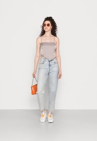 Top de cetim cinza com alças finas, jeans de cintura alta azul claro, ténis brancos com atacadores amarelos e uma bolsa de imitação de couro laranja.