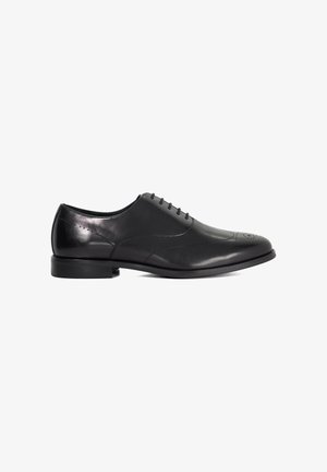 Zwarte leren herenschoen met brogue-details, vetersluiting en lage hak, zijaanzicht op een witte achtergrond.