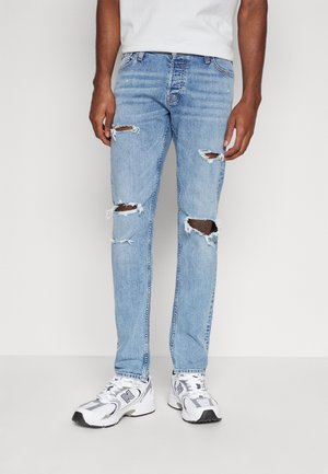 Jean déchiré bleu clair avec des patches distroyés, coupe droite et finition délavée. Assorti à des baskets blanches avec des accents noirs.