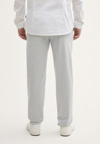Pantalon gris clair avec une coupe droite, fabriqué à partir d'un tissu texturé, associé à des baskets blanches, vu de l'arrière.