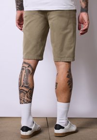Khaki šortky vyrobené z bavlny, ke kolenům, s rovný střih. Mají ploché kapsy a jednoduchý lem. Nošeny s bílými ponožkami a teniskami.
