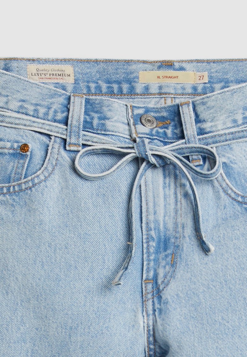 Jeans en denim bleu clair avec une coupe droite, dotés d'un lien à la taille, d'une fermeture à bouton et d'un design standard à 5 poches.