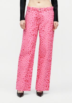 Γυναίκα που φοράει παντελόνι ροζ με κόκκινο λεοπάρ μοτίβο, ψηλόμεσο με φαρδιά μπατζάκια, μαύρες μυτερές γόβες και ένα μαύρο cropped μακρυμάνικο τοπ.