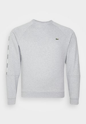 Szara bluza z prążkowanymi mankietami i dekoltem, z małym zielonym logo na piersi oraz białym paskiem bocznym z wzorem tekstowym.