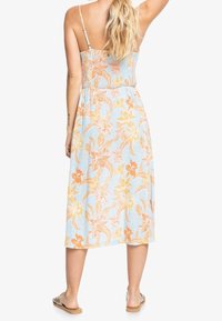 Robe maxi florale en bleu clair, avec des motifs de fleurs orange et jaune, des bretelles spaghetti ajustables et une taille cintrée.