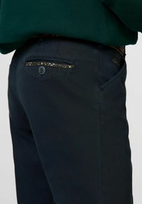 Marineblauwe broek met een gladde textuur, voorzien van een decoratieve achterzaktrim met bloempatroon en een knoopsluiting.