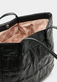 Fekete, steppelt táska dombornyomott logóval, bőr fogantyúkkal és világos rózsaszín béléssel, amely ismétlődő logómintát ábrázol.