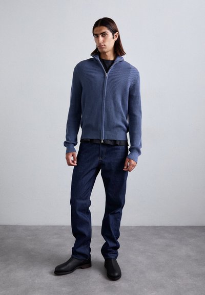 Μπλε ριγωτό cardigan με φερμουάρ, συνδυασμένο με σκούρα τζιν και μαύρες ankle μπότες. Λείος υφασμάτινος κομμωτικός τύπος και εφαρμοστό σχέδιο.