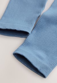 Ærmekanter i blåt ribstrikket stof med en blød tekstur, der har et sømløst design og en let elastik ved åbningerne.