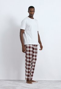 Λευκή κοντομάνικη μπλούζα συνδυασμένη με πιτζάμες σε κόκκινες και λευκές ριγέ. Το ύφασμα φαίνεται μαλακό, με άνετη εφαρμογή και ίσια γραμμή.