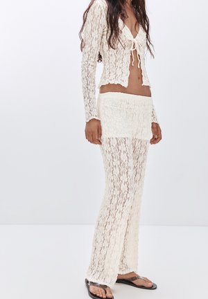 Ensemble deux pièces comprenant un top en dentelle ajusté à manches longues et avec un nœud sur le devant, associé à un pantalon en dentelle assorti, le tout en blanc cassé.