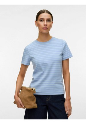 Donna che indossa una camicia a righe a maniche corte azzurro chiaro e pantaloni scuri, che tiene in mano sinistra una pochette morbida marrone con cerniera.