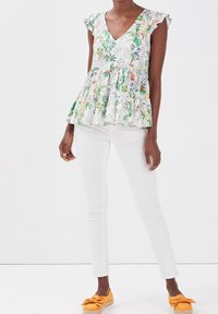 Floral peplum top with a white background, green and colorful botanical patterns, and ruffled sleeves. Paired with white pants and yellow shoes.