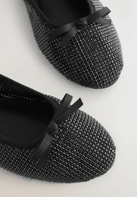 Balerini negre cu ținte, cu suprafață texturată și fundițe mici, pe un fundal alb, prezentate dintr-o perspectivă de sus și din unghi.