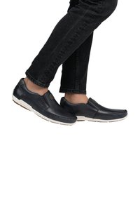 Marineblauwe leren instapschoenen met witte rubberen zolen, voorzien van gestikte details en een platte uitstraling, gedragen met zwarte jeans.