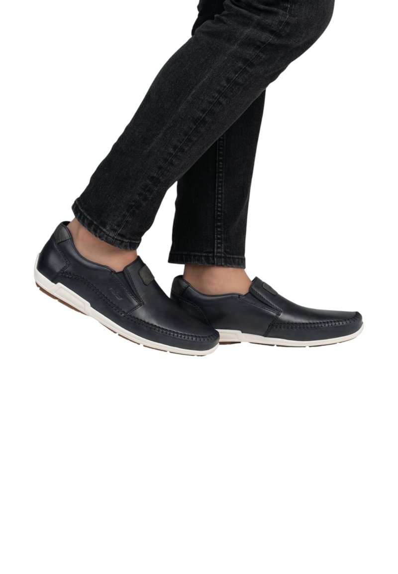 Marineblauwe leren instapschoenen met witte rubberen zolen, voorzien van gestikte details en een platte uitstraling, gedragen met zwarte jeans.