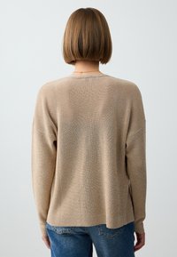 Beige gestrickter Pullover mit lockerer Passform, weiten Ärmeln und geripptem Saum. Verfügt über einen subtilen Glanz und eine weiche Textur.