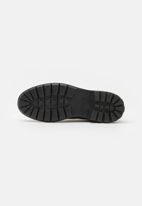 Suela de zapato de goma negra con un profundo relieve, con forma redondeada y superficie texturizada. Se puede ver un logo grabado en el lateral.