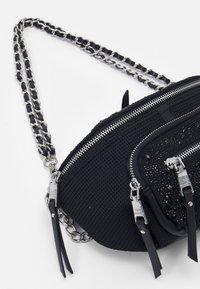 Černá taška s texturovanou tkaninou, stříbrnými zipovými detaily a řetízkovým popruhem. Obsahuje hladkou, lesklou část zdobenou černými flitry.