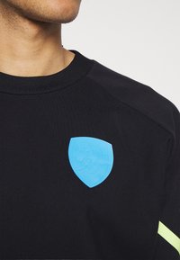 Felpa nera con un logo in gomma blu dell'Arsenal sul petto. Include un collo a costine e dettagli in giallo neon sulle maniche.