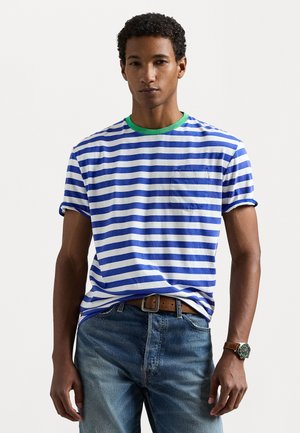 T-shirt rayé bleu et blanc avec un col côtelé vert, présentant une poche sur le devant. Porté avec un jean en denim bleu et une montre en cuir brun.