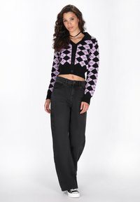 Avkortad svart argyle-kofta med rosa diamanter, framsluttningsknappar och V-ringning, i kombination med högmidjade svarta vida jeans och sneakers.