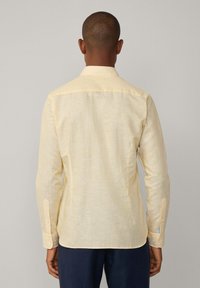 Camicia a maniche lunghe giallo chiaro con un sottile motivo a righe, colletto button-down e polsini standard. Tessuto in cotone con una consistenza liscia.