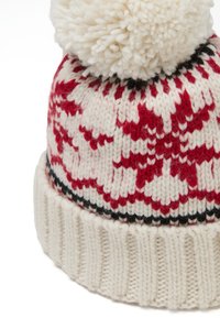 Cappello invernale lavorato a maglia di colore crema con motivi rossi e dettagli neri. Presenta un grande pom-pom bianco e strutturato sulla parte superiore e un bordo a coste.
