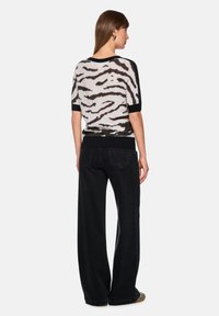 Schwarz-weißer Pullover mit tierischem Muster und kurzen Ärmeln, schwarzer, einfarbiger Besatz, kombiniert mit hochtaillierten schwarzen Jeans mit weitem Bein.