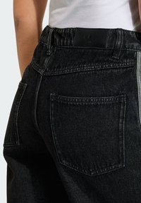 Τα μαύρα τζιν από денιμ διαθέτουν ψηλή μέση με μαύρο δερμάτινο ταμπελάκι, πίσω τσέπες και γκρι ρίγες στο πλάι. Το ύφασμα έχει απαλή υφή.