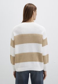 Gestrickter Pullover in Weiß und Beige gestreift, mit lockerem Schnitt, weiten Ärmeln und gerippten Bündchen. Sichtbare Struktur im Strickmuster.