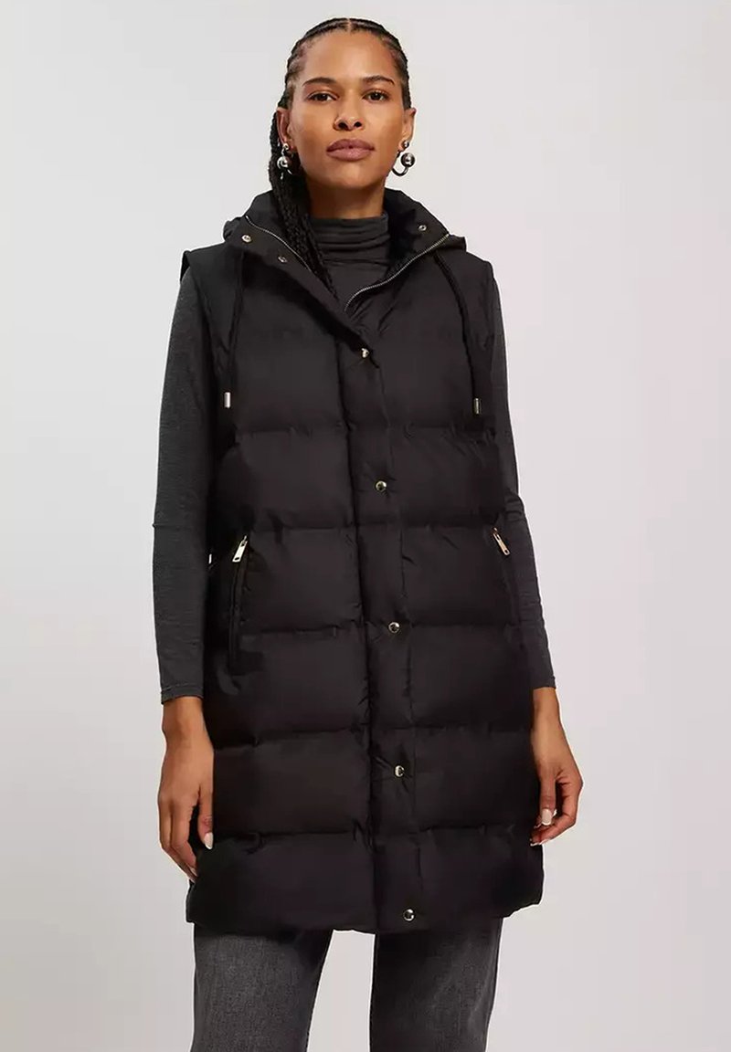 Czarna kamizelka puchowa z kapturem, z zamkiem błyskawicznym i zapięciem na napy, bocznymi kieszeniami oraz pikowaną fakturą. Wytrzymały materiał, sięgająca do kolan konstrukcja.