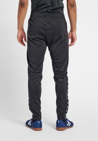 Zwarte sportieve joggings met een elastische tailleband, taps toelopende pasvorm en zijstrepen. Gekleed met blauwe sportschoenen met bruine zolen.