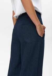 Dark blue denim pants with a straight-leg design, featuring back pockets and a high waistband. Fabric has a smooth, textured finish.