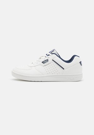 Scarpa sportiva bianca con pannelli perforati, accenti blu navy e suola in gomma piatta. Presenta una chiusura con lacci e un dettaglio con il logo sul lato.