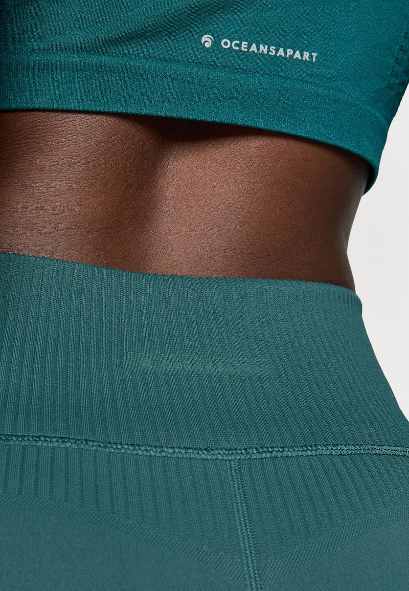 Top deportivo corto color teal y leggings de tiro alto exhibidos, con textura acanalada, diseño sin costuras y detalle del logo sutil en la cintura.