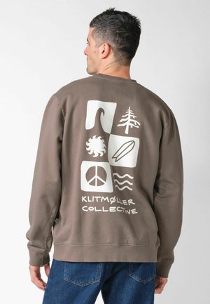 Homme portant un sweat-shirt marron avec des symboles blancs sur le thème de la nature et le texte « Klitmøller Collective » au dos, tourné vers l'arrière sur un fond uni.